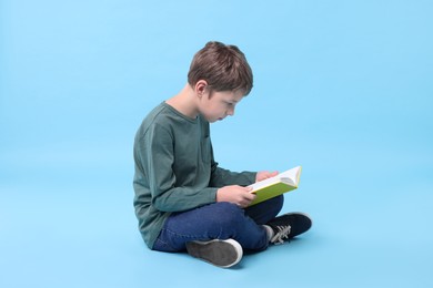 Photo of Boy with incorrect posture reading book on light blue background