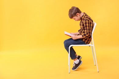 Boy with incorrect posture reading book on chair against yellow background