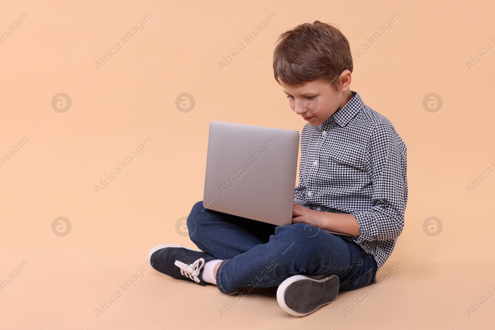 Photo of Boy with incorrect posture and laptop sitting on beige background