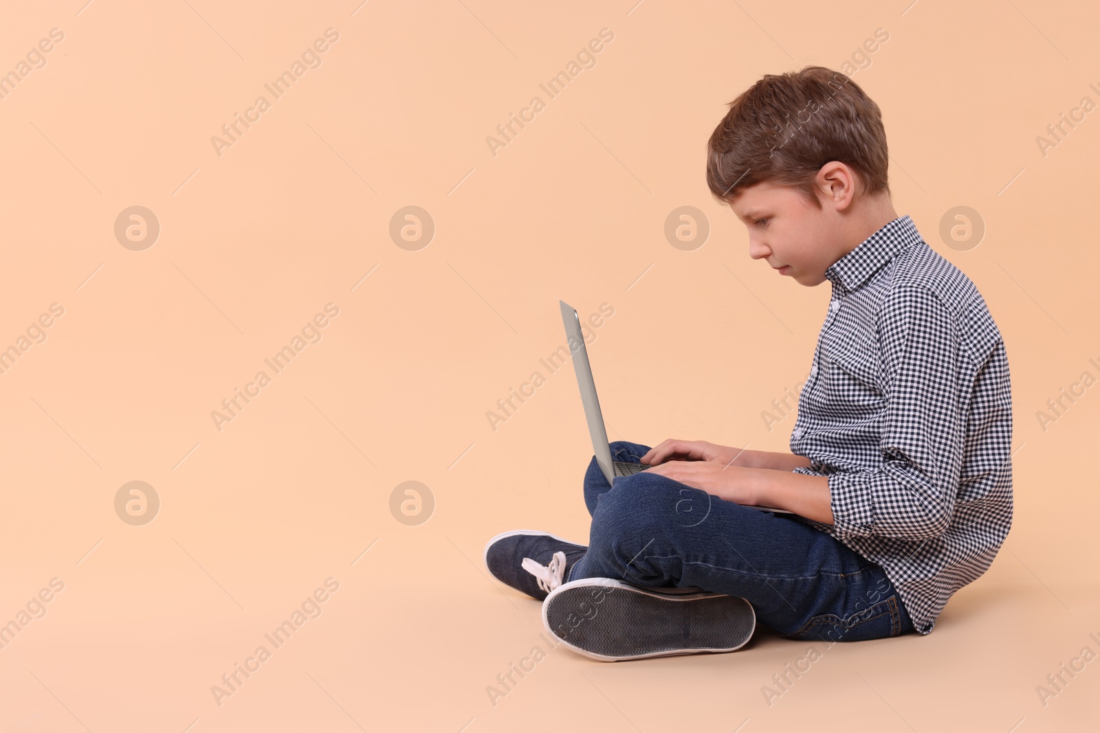 Photo of Boy with incorrect posture and laptop sitting on beige background