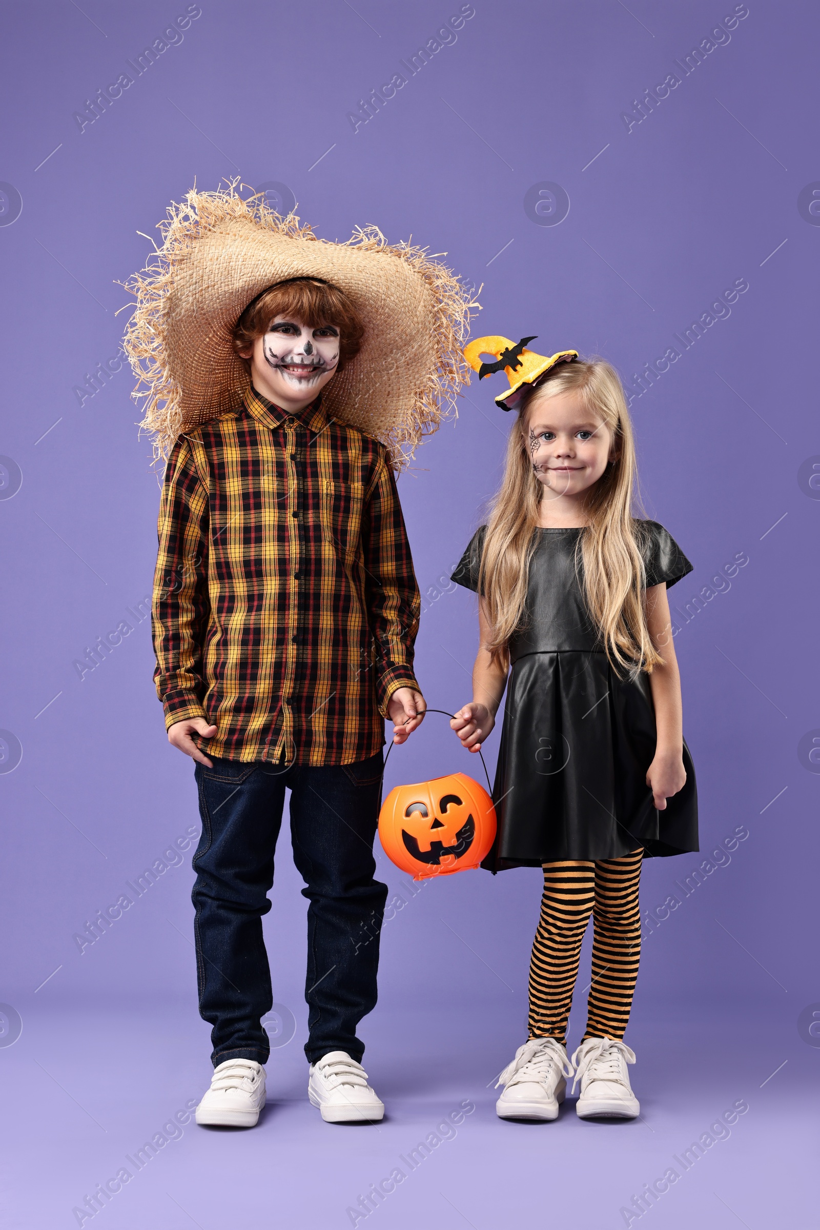 Photo of Cute children with pumpkin bucket wearing costumes on violet background. Halloween celebration