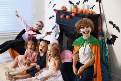 Photo of Funny children wearing costumes for Halloween celebration in room, selective focus