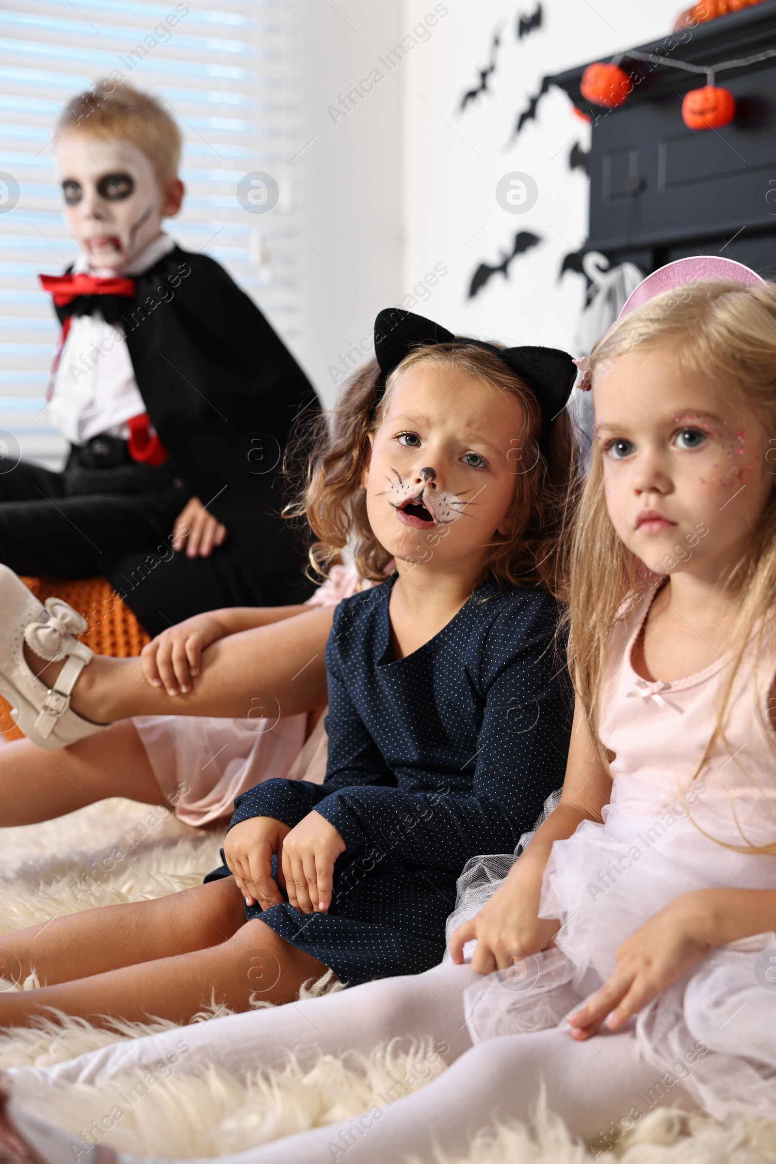 Photo of Funny children wearing costumes for Halloween celebration in room, selective focus