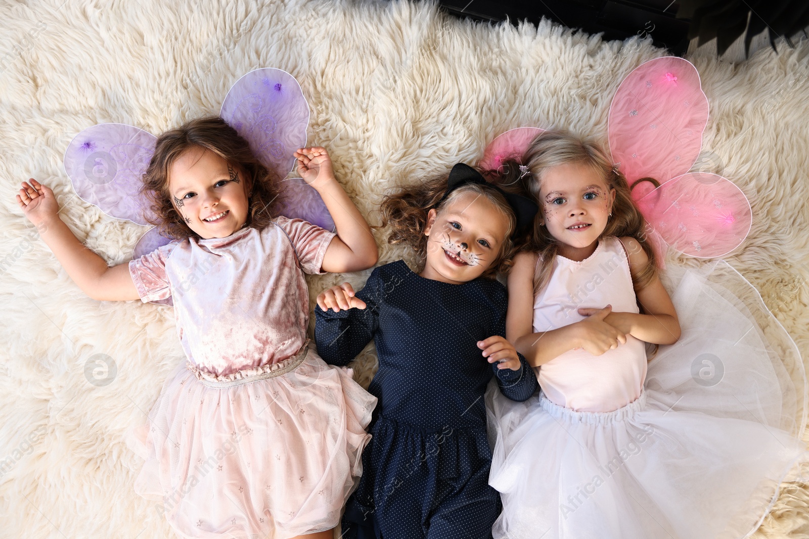 Photo of Cute girls wearing costumes on soft rug, top view. Halloween celebration