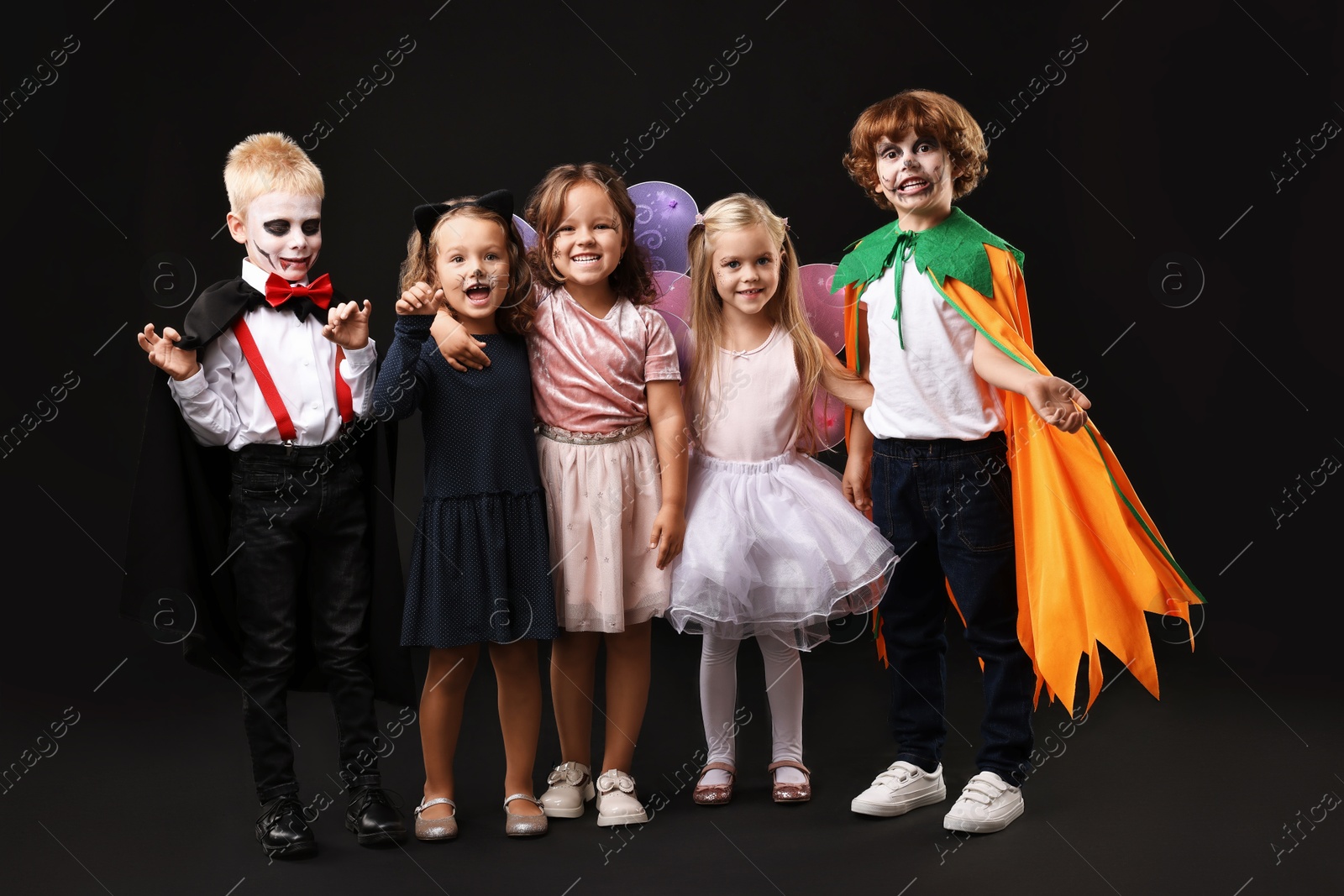 Photo of Funny children wearing costumes for Halloween celebration on black background