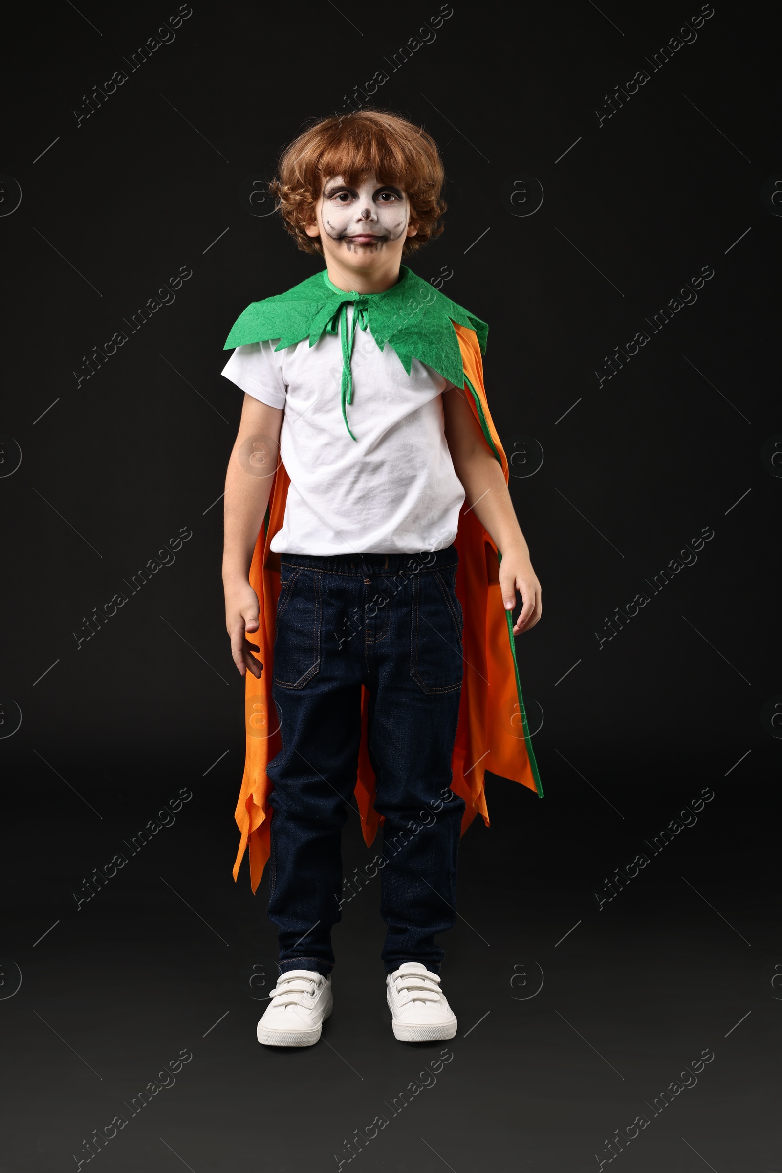 Photo of Cute boy dressed like pumpkin for Halloween celebration on black background