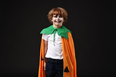 Cute boy dressed like pumpkin for Halloween celebration on black background