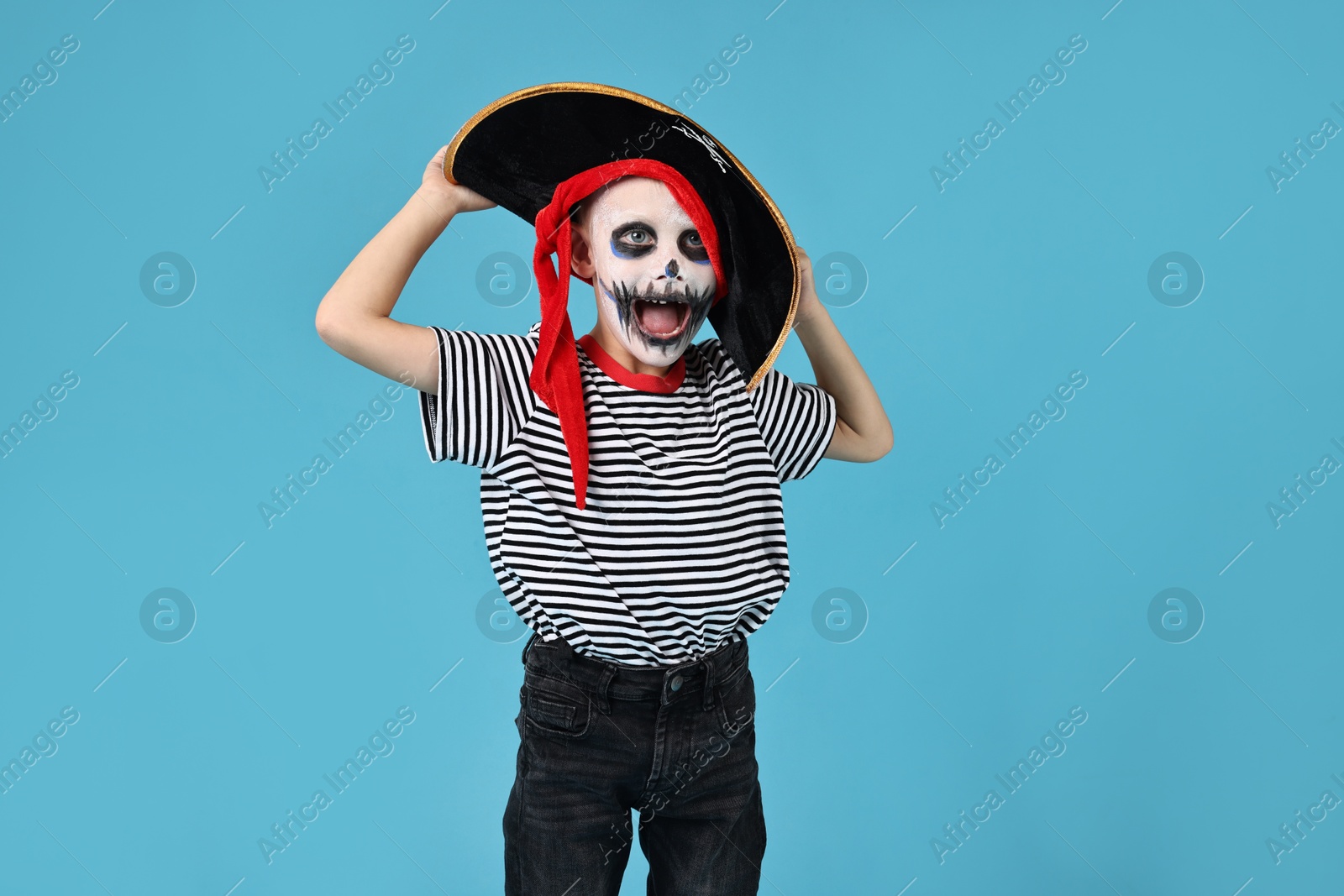 Photo of Funny boy dressed like pirate on light blue background. Halloween costume