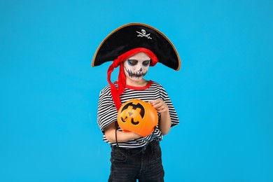 Funny boy with pumpkin bucket dressed like pirate on light blue background. Halloween costume