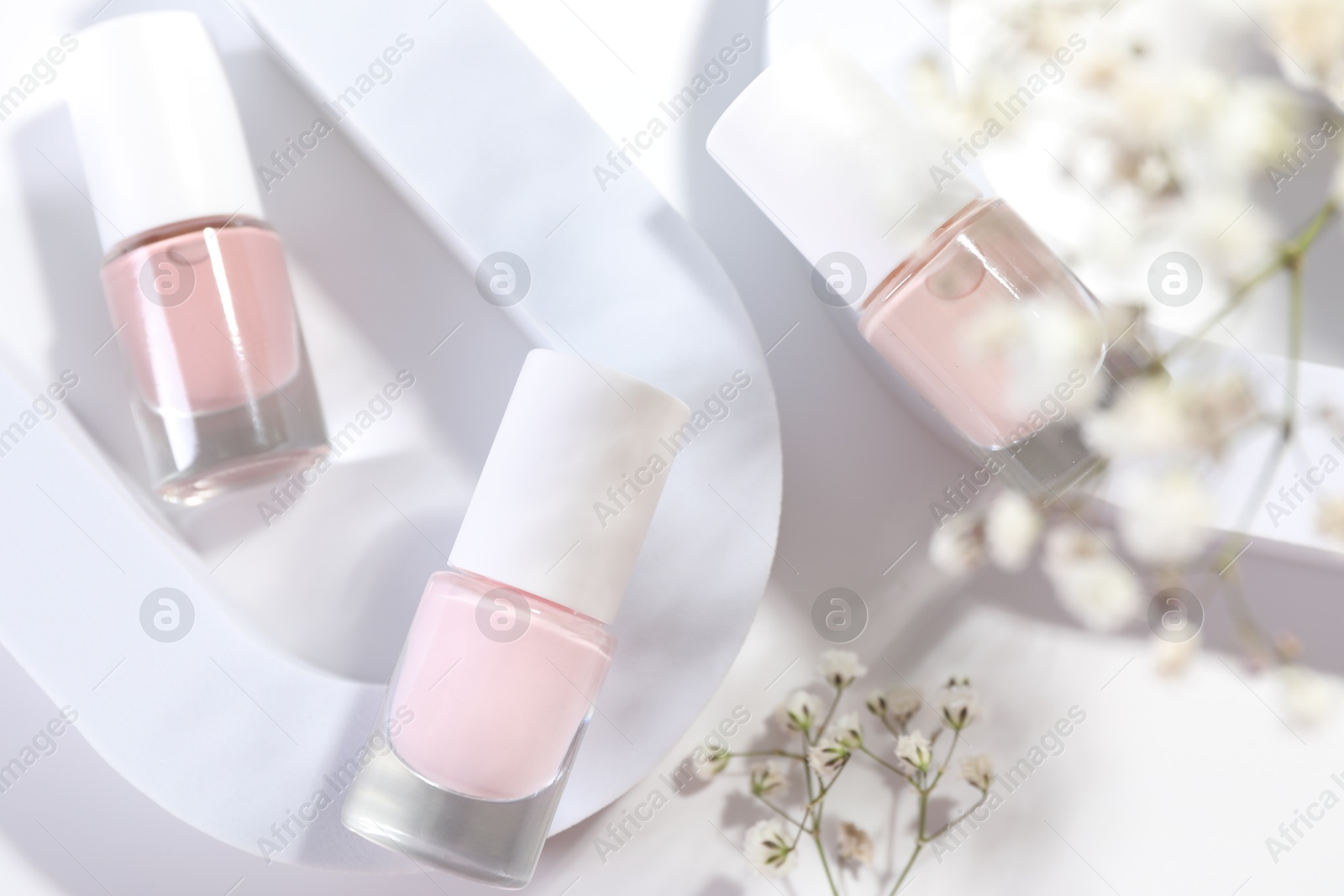 Photo of Nail polishes in bottles and gypsophila flowers on white background, flat lay