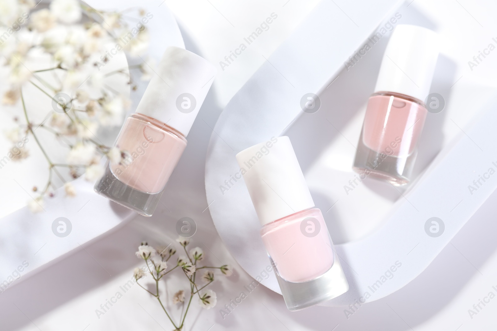 Photo of Nail polishes in bottles and gypsophila flowers on white background, flat lay