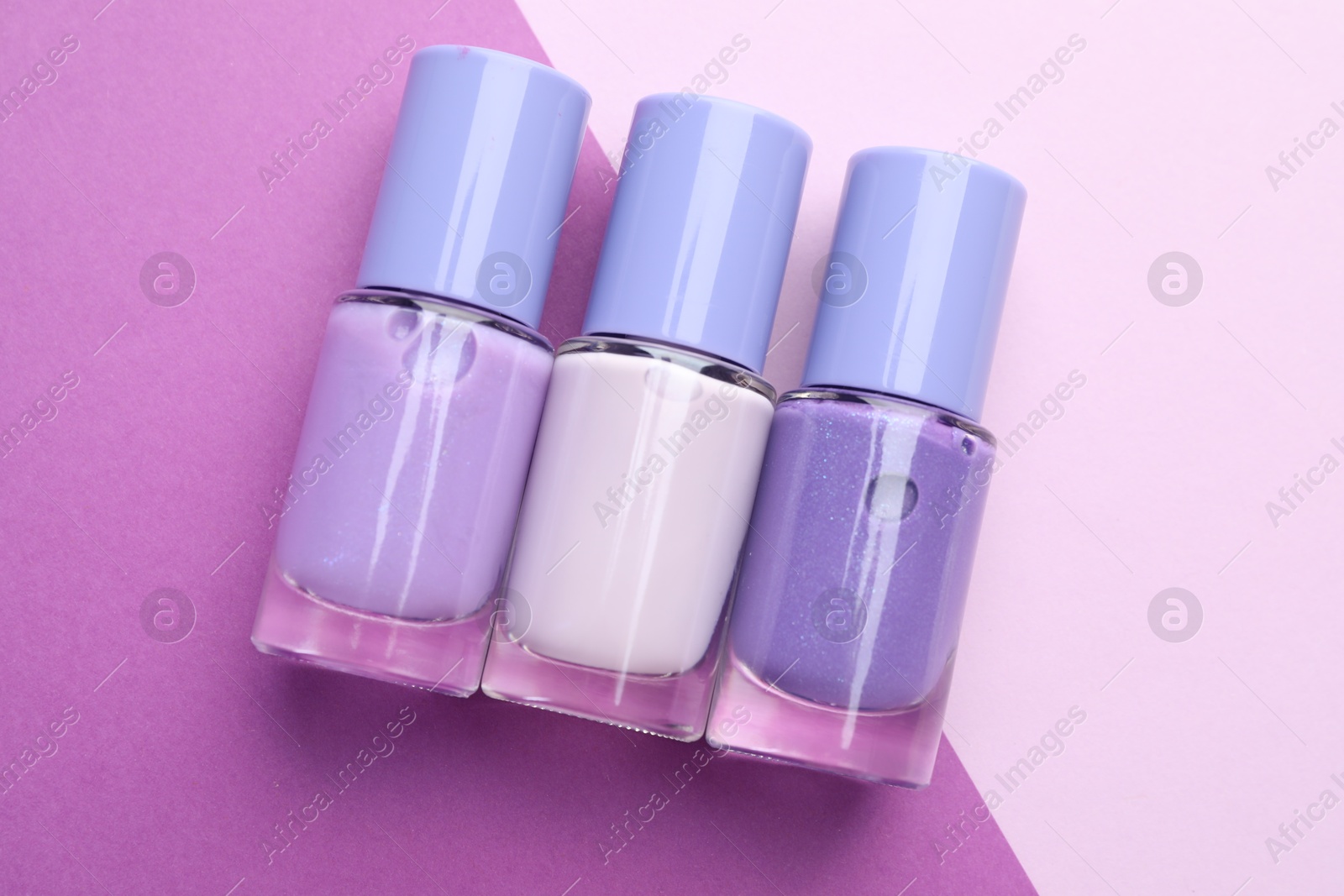 Photo of Nail polishes in bottles on color background, flat lay