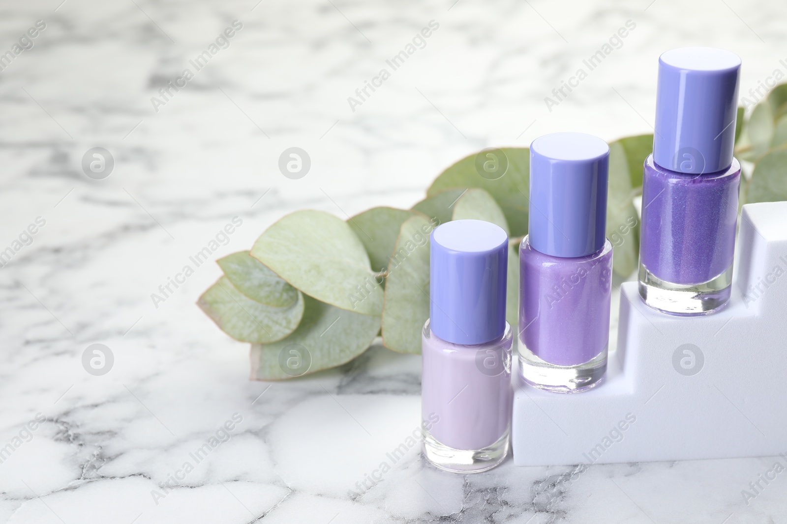 Photo of Nail polishes in bottles and eucalyptus branch on white marble table, space for text