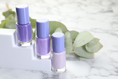 Photo of Nail polishes in bottles and eucalyptus branch on white marble table, space for text