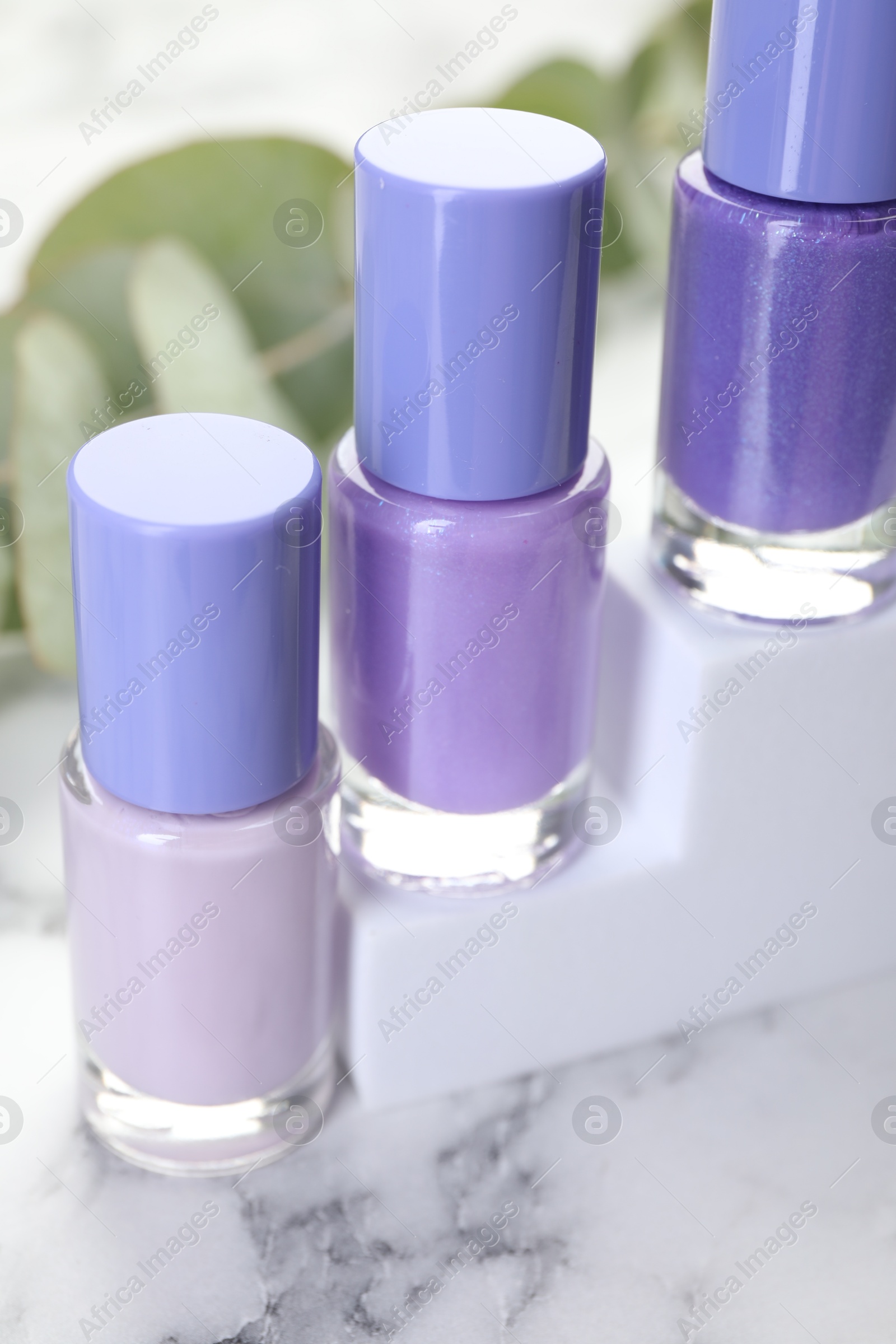 Photo of Nail polishes in bottles on white marble table, closeup