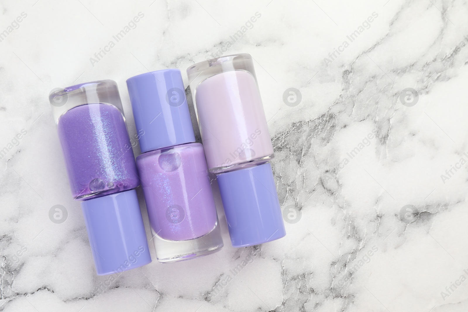 Photo of Nail polishes in bottles on white marble background, flat lay. Space for text