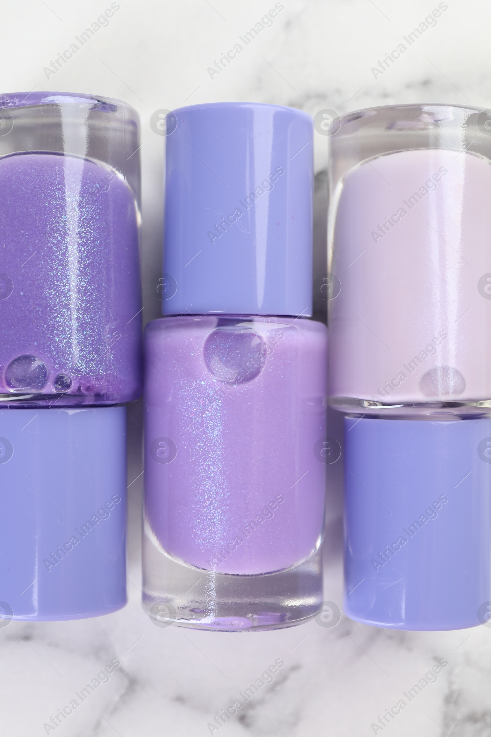 Photo of Nail polishes in bottles on white marble background, flat lay