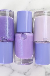 Photo of Nail polishes in bottles on white marble background, flat lay