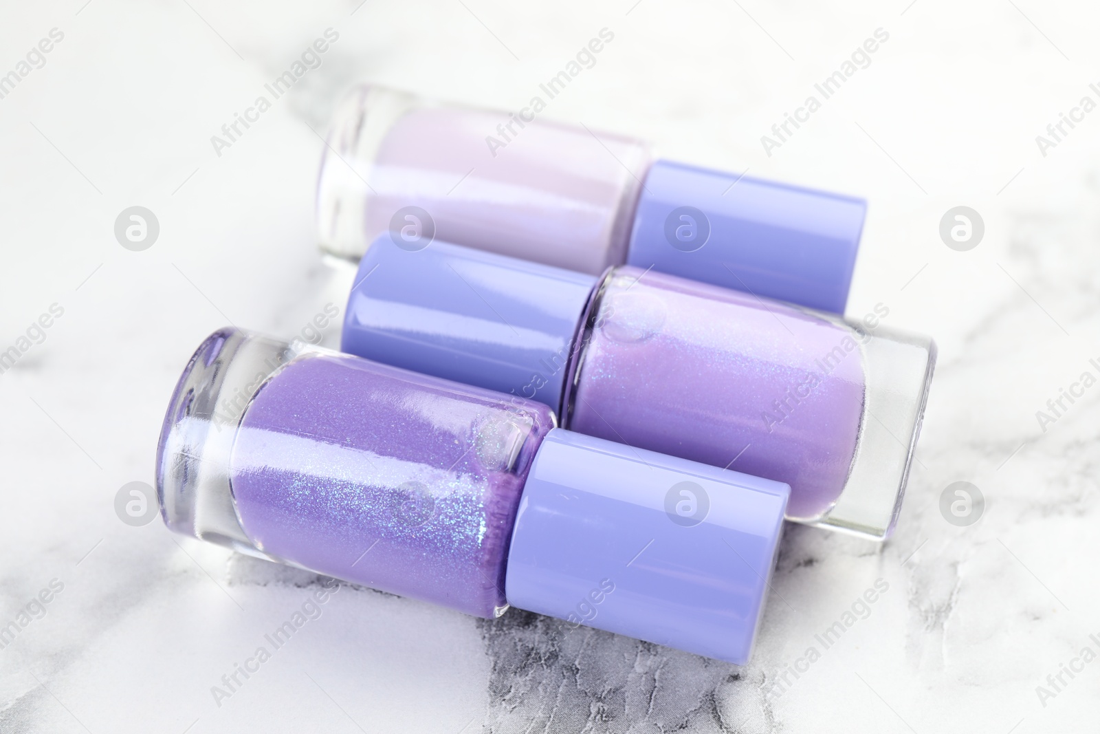 Photo of Nail polishes in bottles on white marble table, closeup