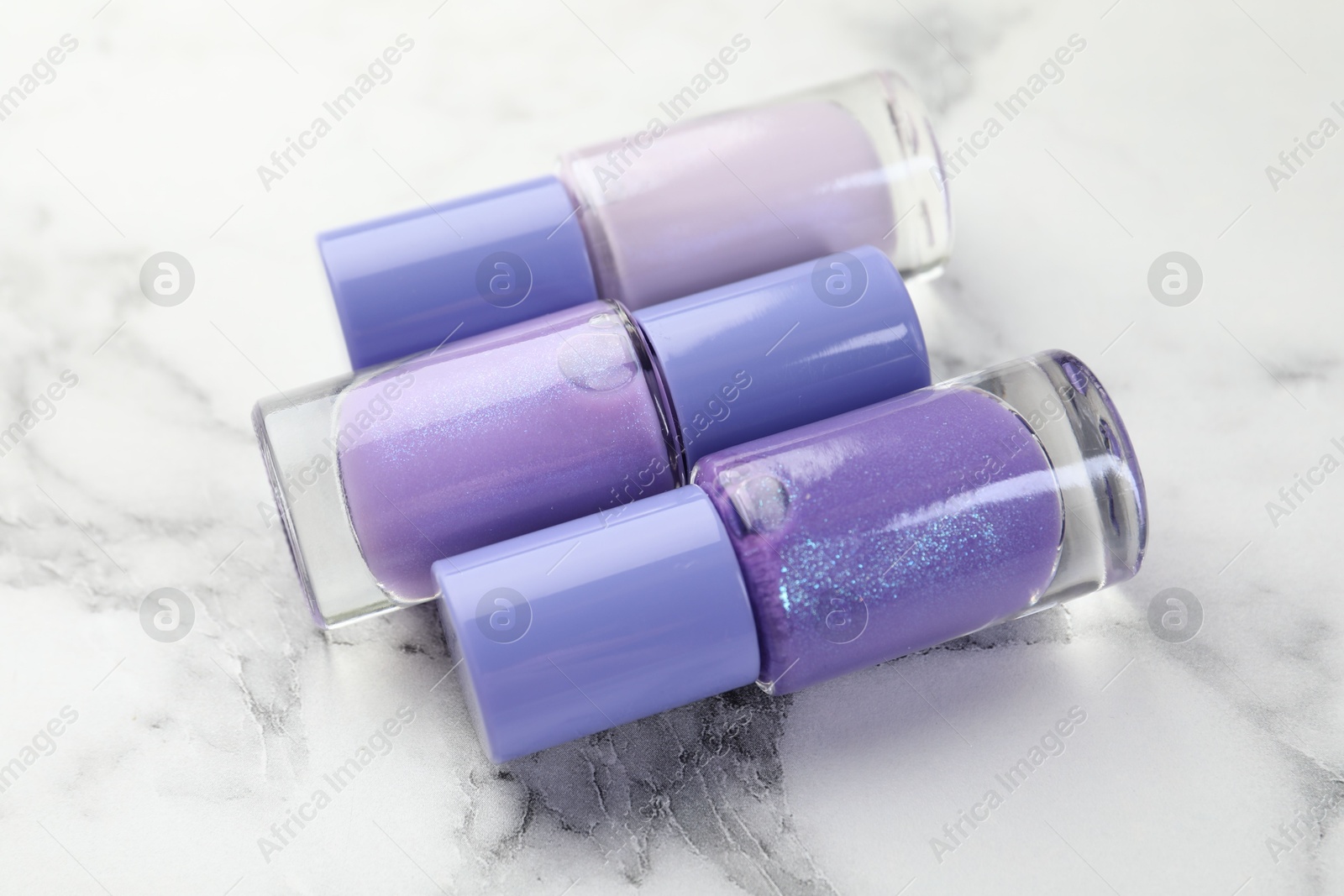 Photo of Nail polishes in bottles on white marble table, closeup