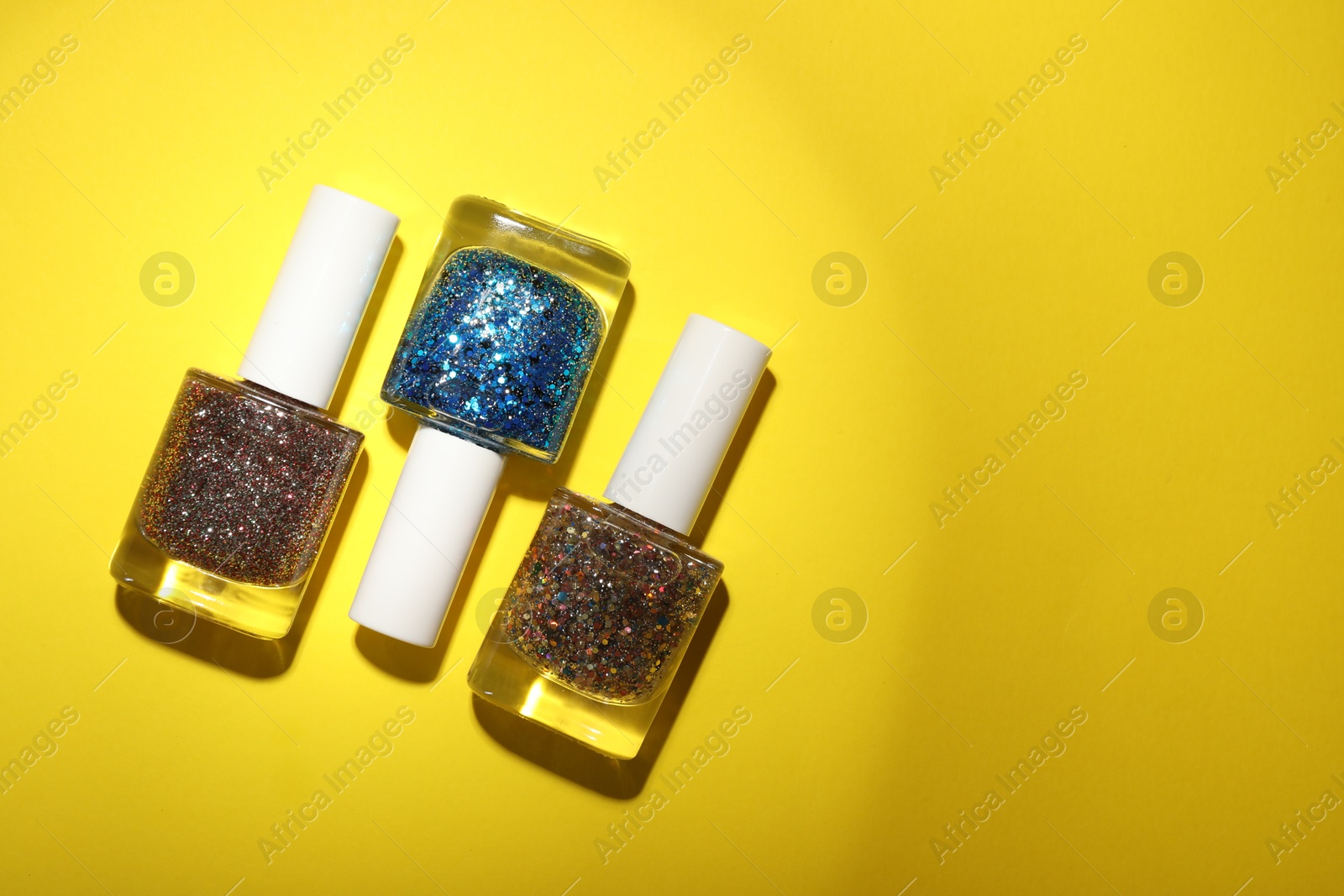 Photo of Nail polishes in bottles on yellow background, flat lay. Space for text