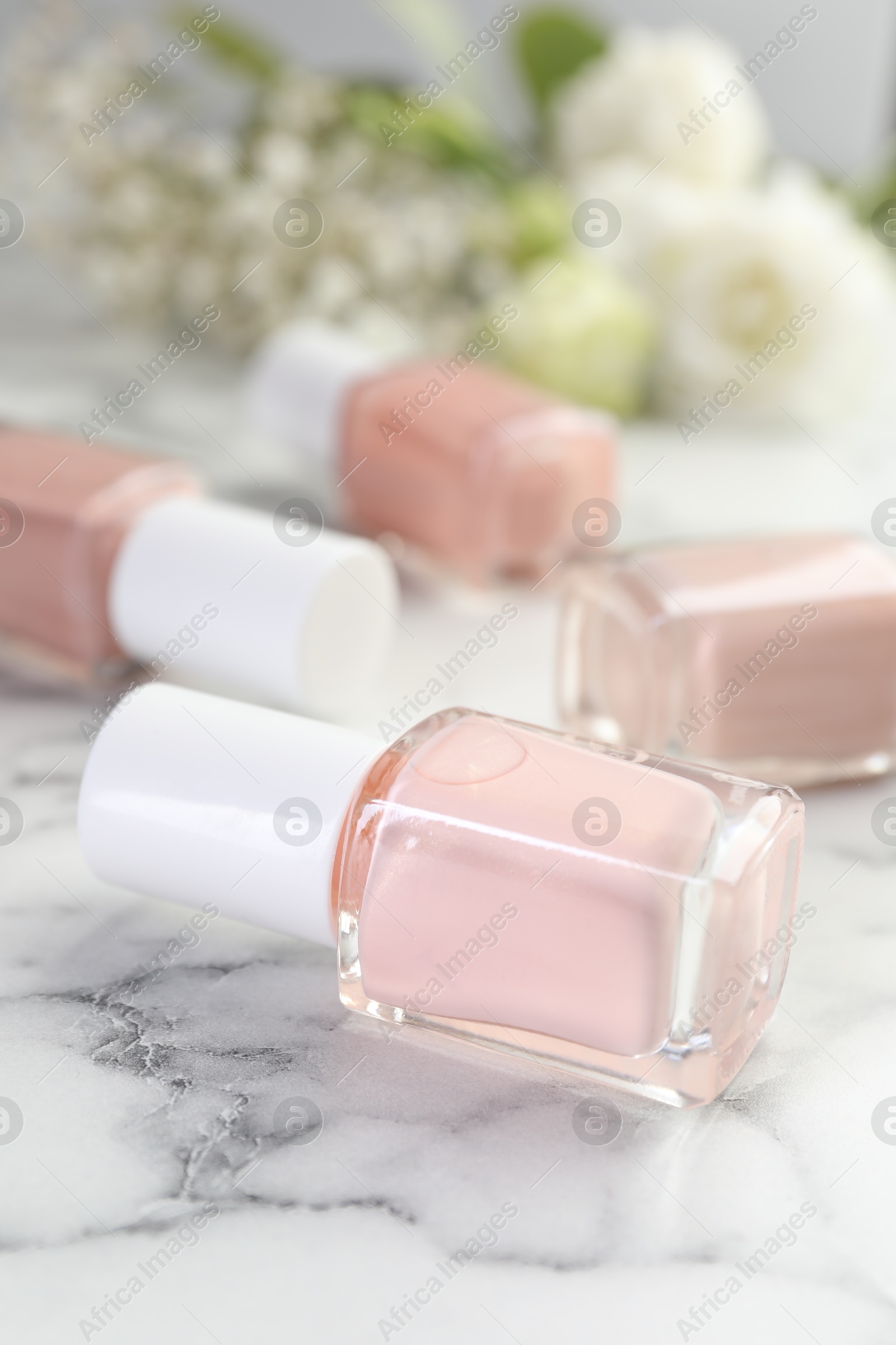 Photo of Nail polishes in bottles on white marble table, closeup