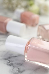 Photo of Nail polishes in bottles on white marble table, closeup