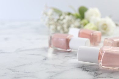 Photo of Nail polishes in bottles on white marble table, closeup. Space for text