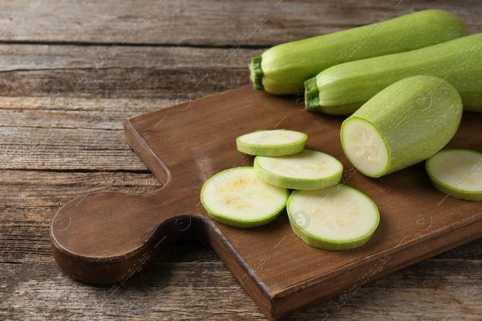 Photo of Board with fresh zucchinis on wooden table