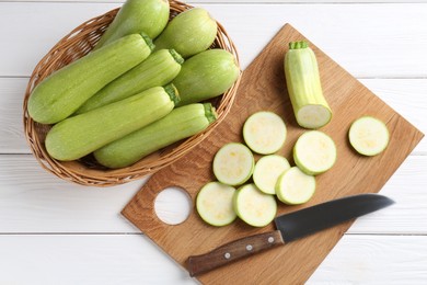 Photo of Fresh zucchinis and knife on white wooden table, flat lay