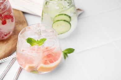 Different refreshing drinks in glasses on white tiled table, space for text