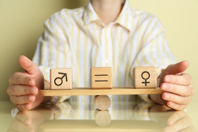 Gender equality concept. Woman with wooden cubes of male and female symbols on scales at table, closeup