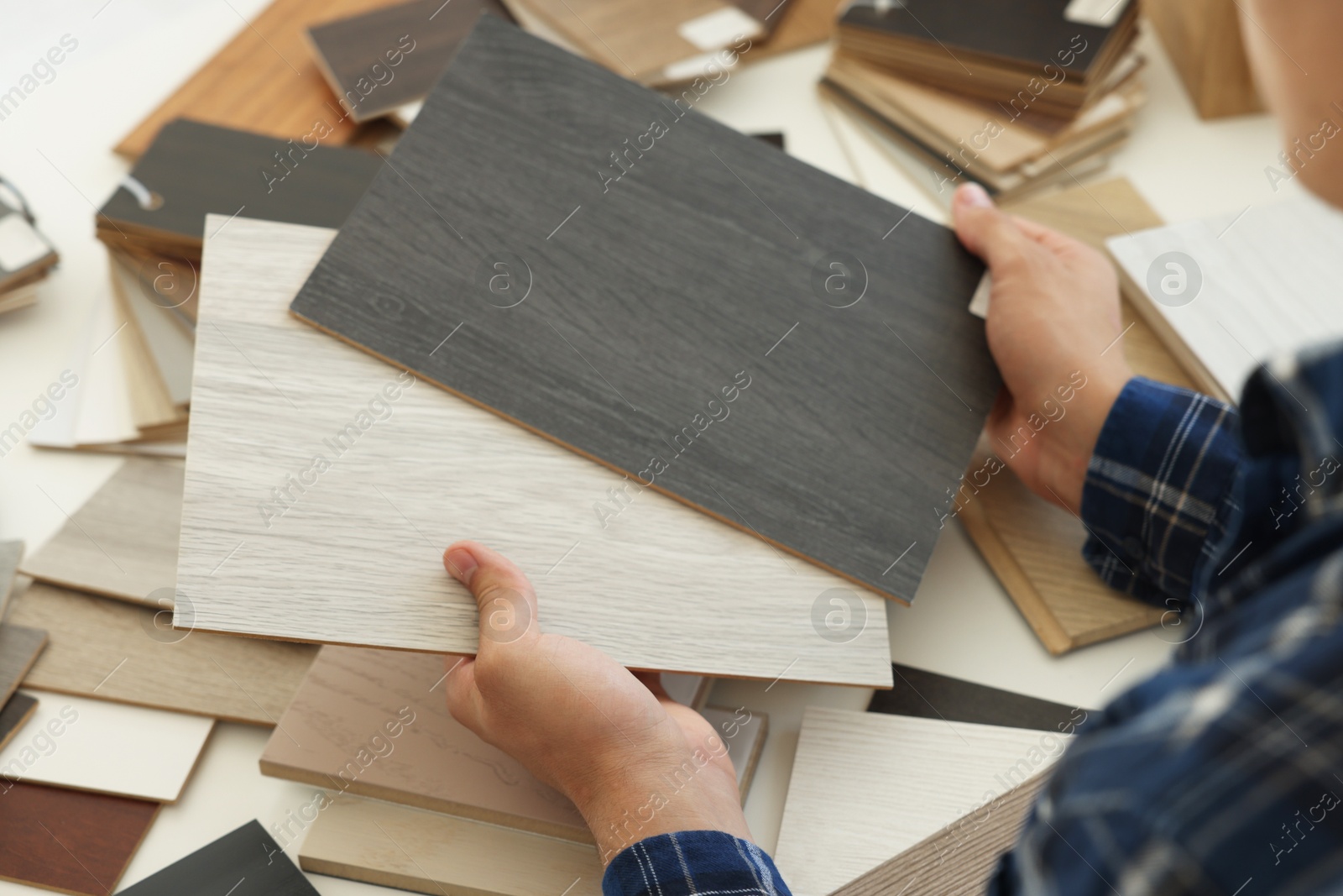 Photo of Man choosing wooden flooring among different samples at table, closeup