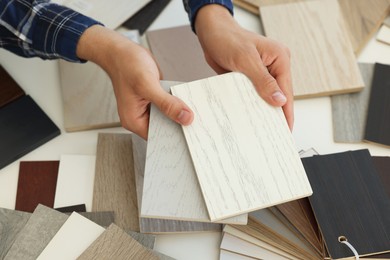 Photo of Man choosing wooden flooring among different samples at table, closeup