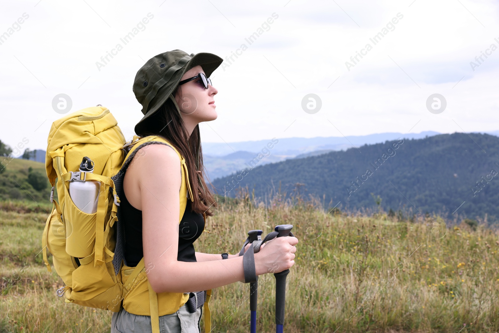 Photo of Young hiker with backpack and trekking poles in mountains, space for text