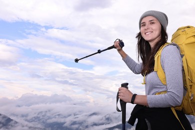 Young hiker with trekking poles and backpack in mountains outdoors, space for text