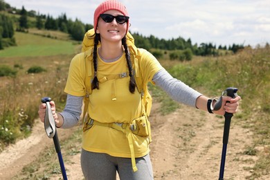 Young hiker with sunglasses, trekking poles and backpack outdoors