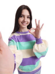 Photo of Smiling teenage girl showing OK gesture while taking selfie on white background