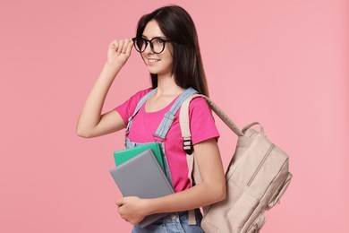 Photo of Portrait of cute teenage girl with backpack and books on pink background