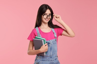 Portrait of cute teenage girl with books on pink background