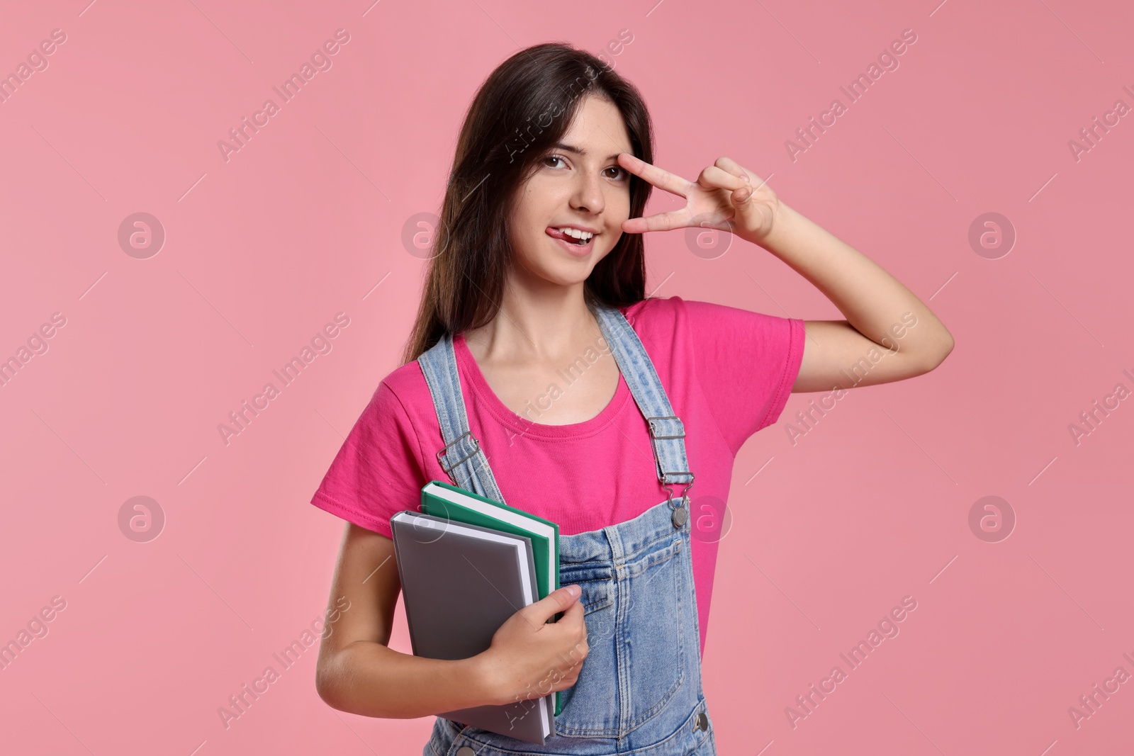 Photo of Portrait of cute teenage girl with books on pink background