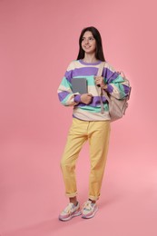 Photo of Cute teenage girl with backpack and book on pink background