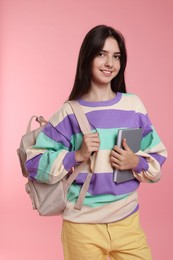 Photo of Cute teenage girl with backpack and book on pink background