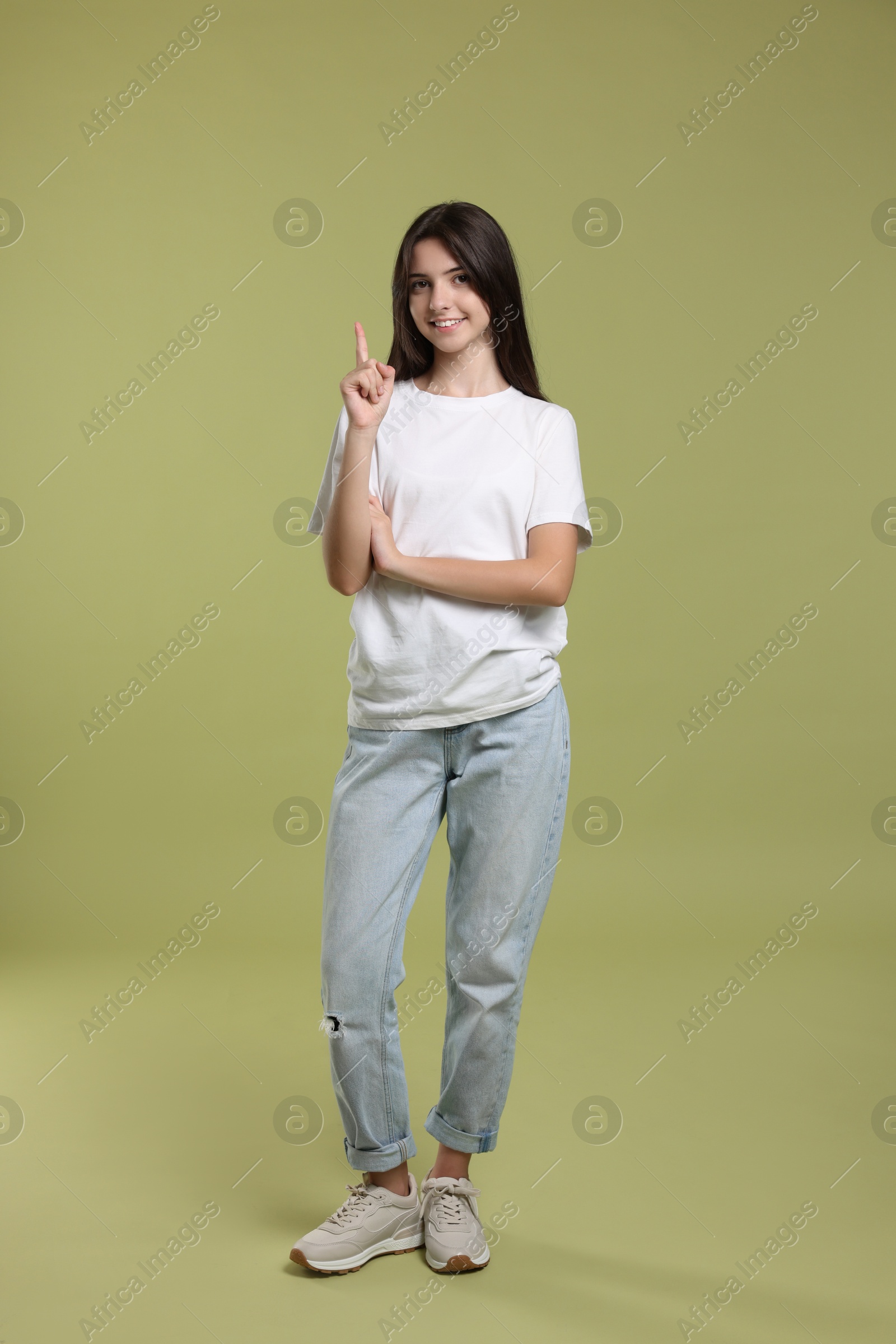 Photo of Cute teenage girl pointing at something on olive background