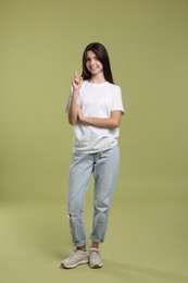 Photo of Cute teenage girl pointing at something on olive background