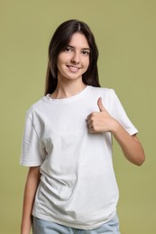 Portrait of cute teenage girl showing thumbs up on olive background