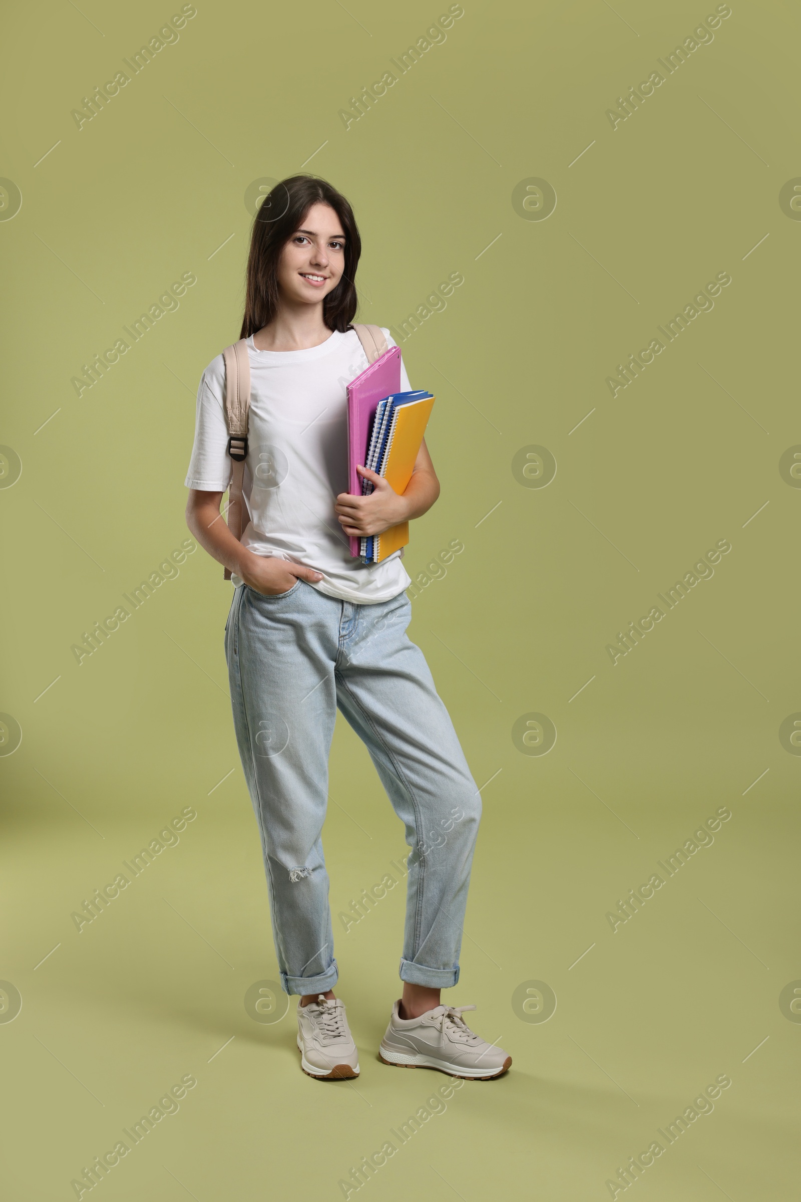 Photo of Cute teenage girl with backpack and books on olive background