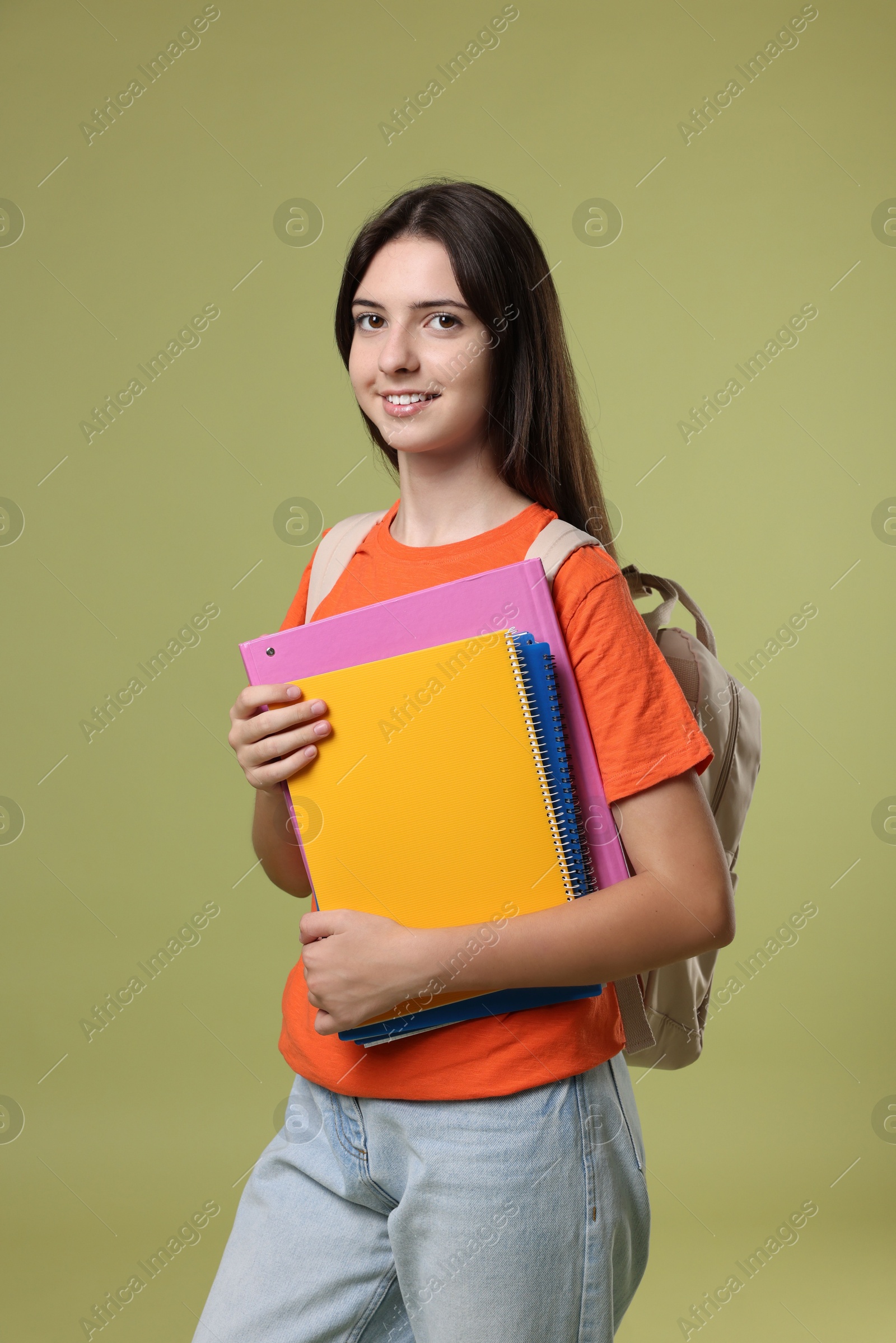 Photo of Portrait of cute teenage girl with backpack and books on olive background