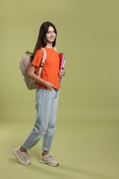 Photo of Cute teenage girl with backpack and books on olive background