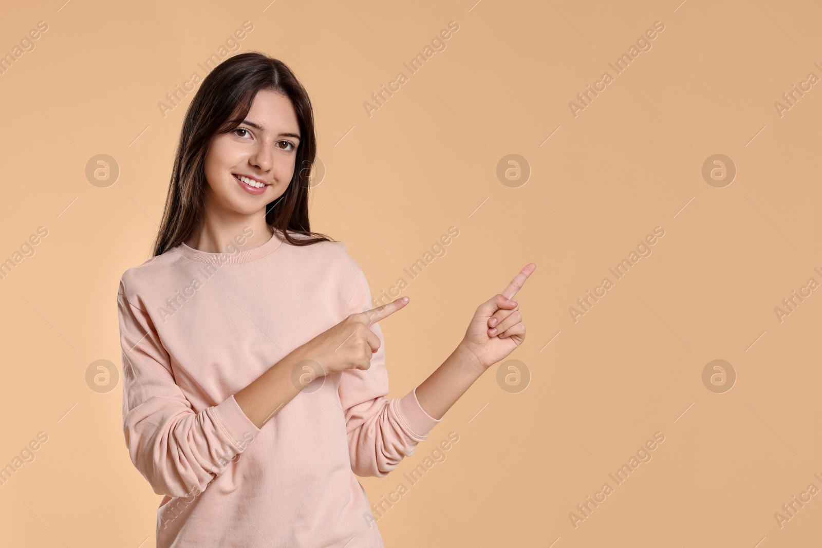 Photo of Portrait of cute teenage girl pointing at something on beige background. Space for text